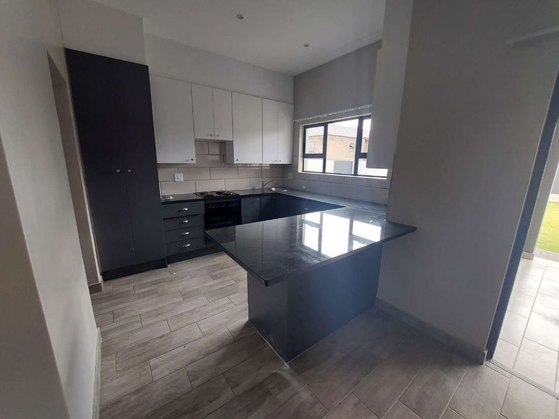 Modern kitchen featuring two-tone cabinetry, granite countertops, integrated hob and oven, and tiled flooring with a breakfast nook peninsula.
