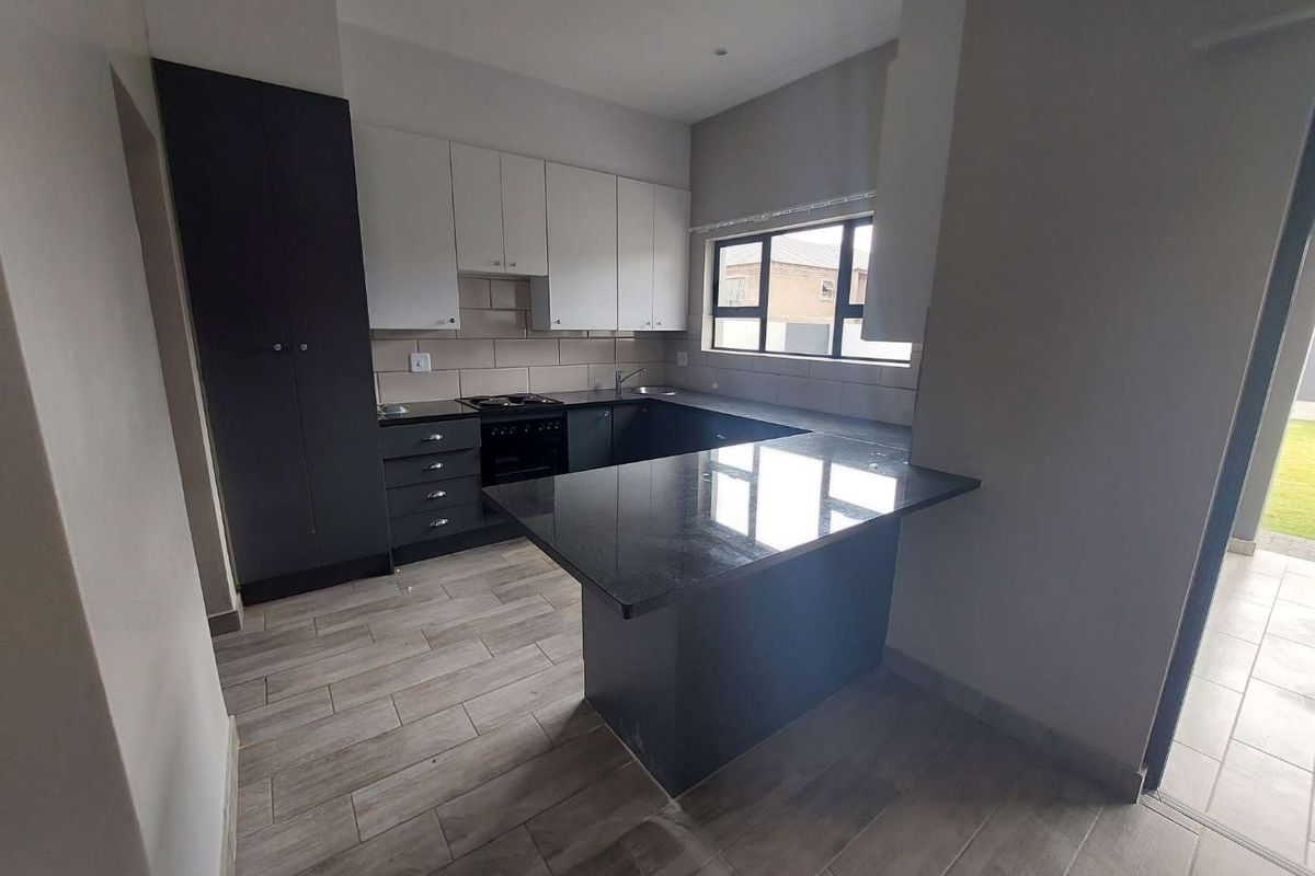 Modern kitchen featuring two-tone cabinetry, granite countertops, integrated hob and oven, and tiled flooring with a breakfast nook peninsula.