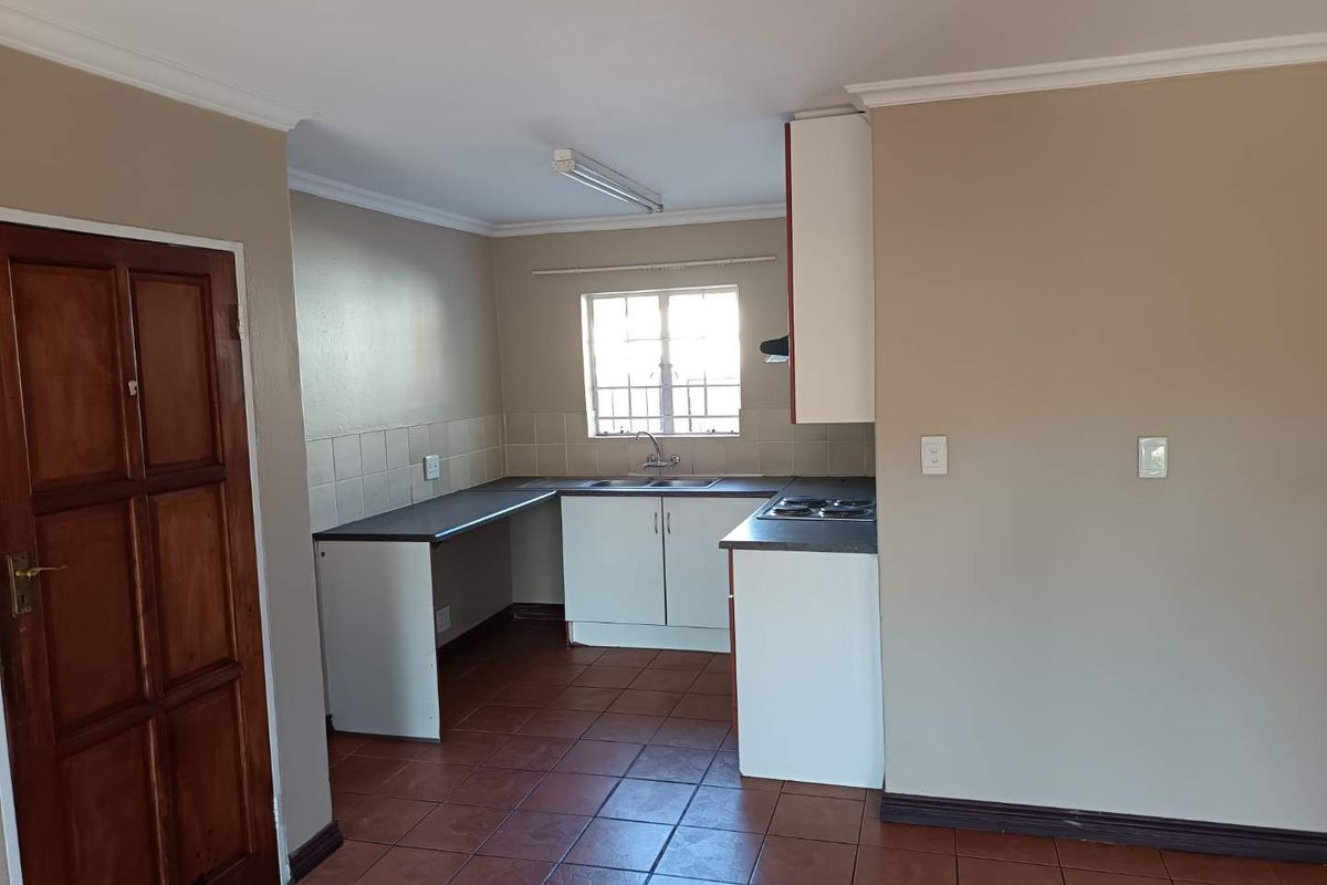 A functional, empty kitchen featuring laminate countertops, built-in cabinetry, an electric hob, and tiled flooring, offering a blank canvas for potential updates.