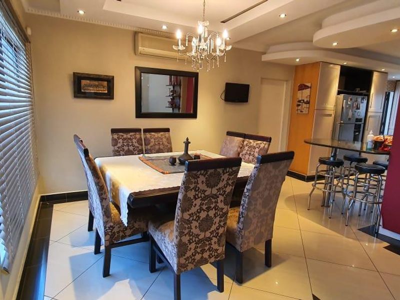 Open-plan dining and kitchen area featuring tiled flooring, recessed ceiling details, a breakfast bar, and integrated cabinetry with modern lighting fixtures.
