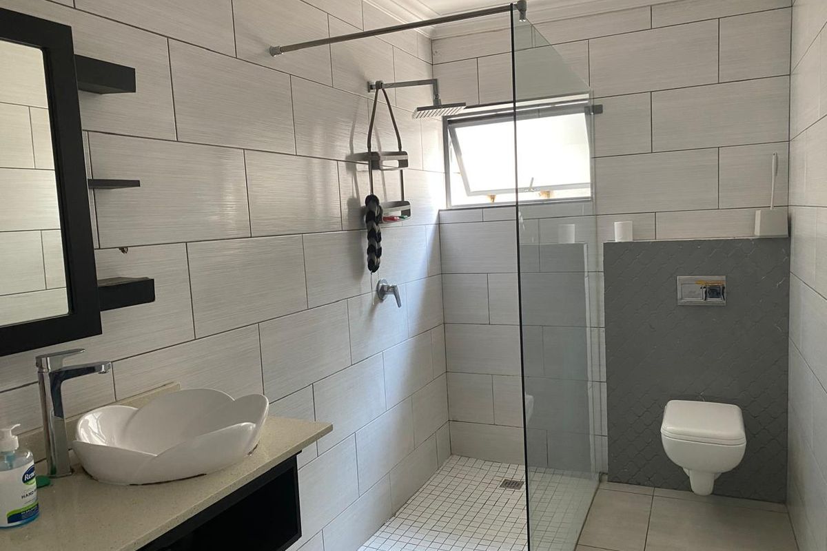 Modern bathroom featuring a walk-in glass shower, wall-mounted toilet, and a stylish vessel sink set on a stone vanity countertop.