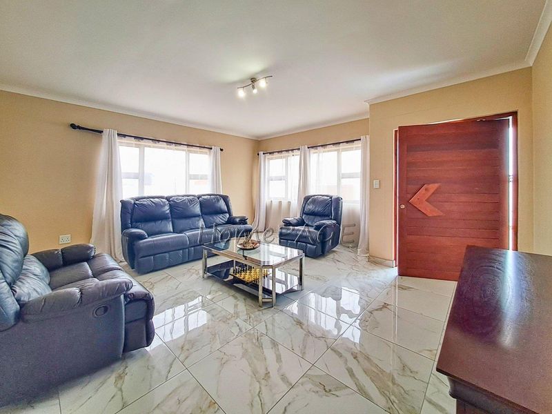 Spacious living room featuring polished marble-look floor tiles, solid timber entrance door, and large windows providing ample natural light.