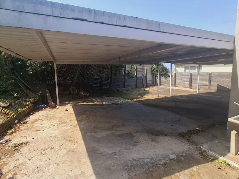 A large outdoor carport area with a metal roof structure and concrete flooring, providing ample covered parking space.