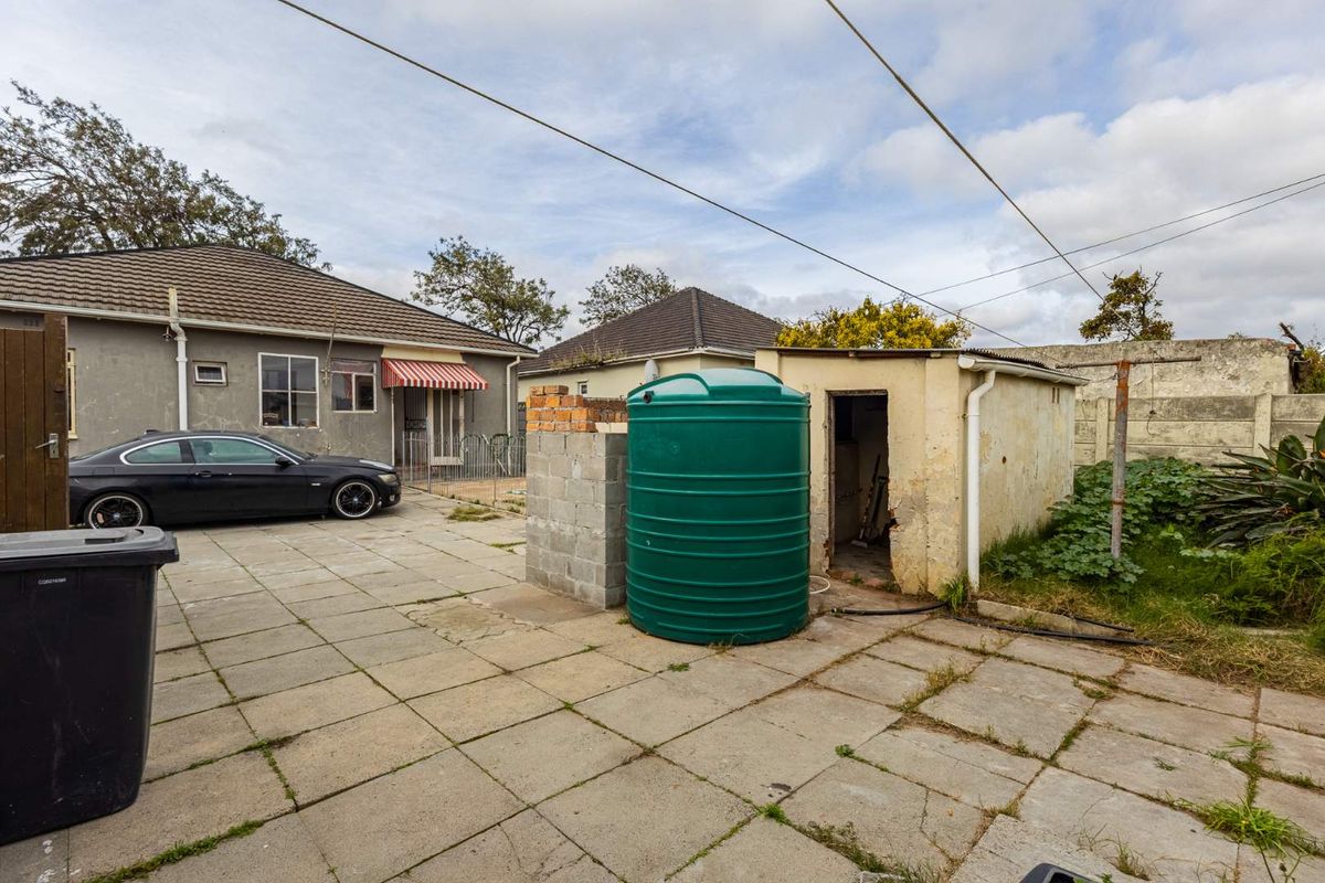 Rear exterior area featuring a paved courtyard, a water storage tank, and a small utility outbuilding requiring maintenance.