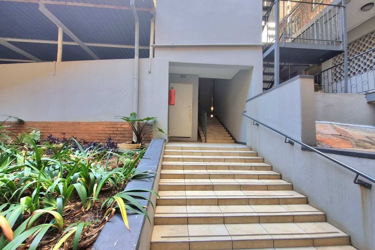 Exterior view of a communal apartment staircase with tiled steps, metal handrails, and adjacent landscaped garden area.