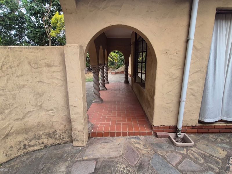 Covered patio area featuring distinctive arched colonnade with spiral columns and terracotta tile flooring, leading to a stone-paved outdoor space.