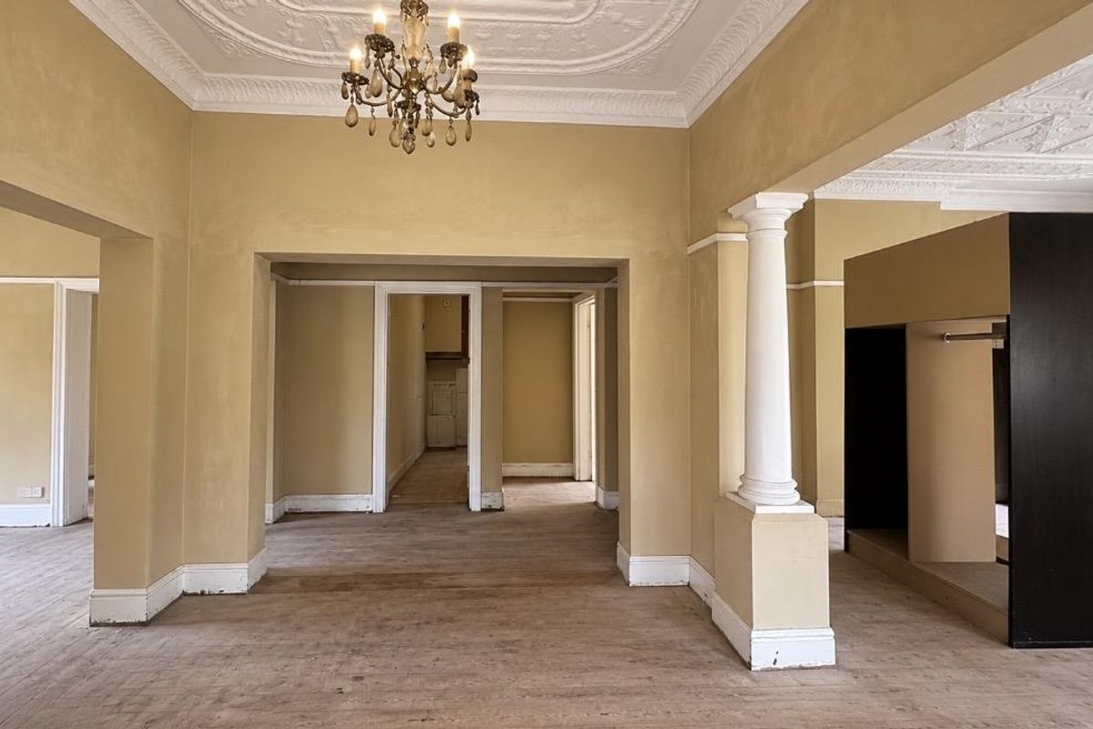 Spacious living area featuring ornate ceiling detailing, a classical column, and hardwood flooring, offering an open-plan layout with multiple access points to adjacent rooms.