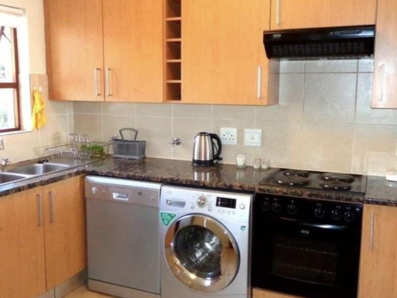 Functional kitchen featuring light wood cabinetry, granite countertops, built-in oven, electric hob, and tiled backsplash with integrated appliance spaces.