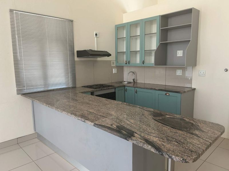 A clean, functional kitchen featuring granite countertops, fitted cabinetry, built-in appliances, and tiled flooring, offering a practical layout for daily use.