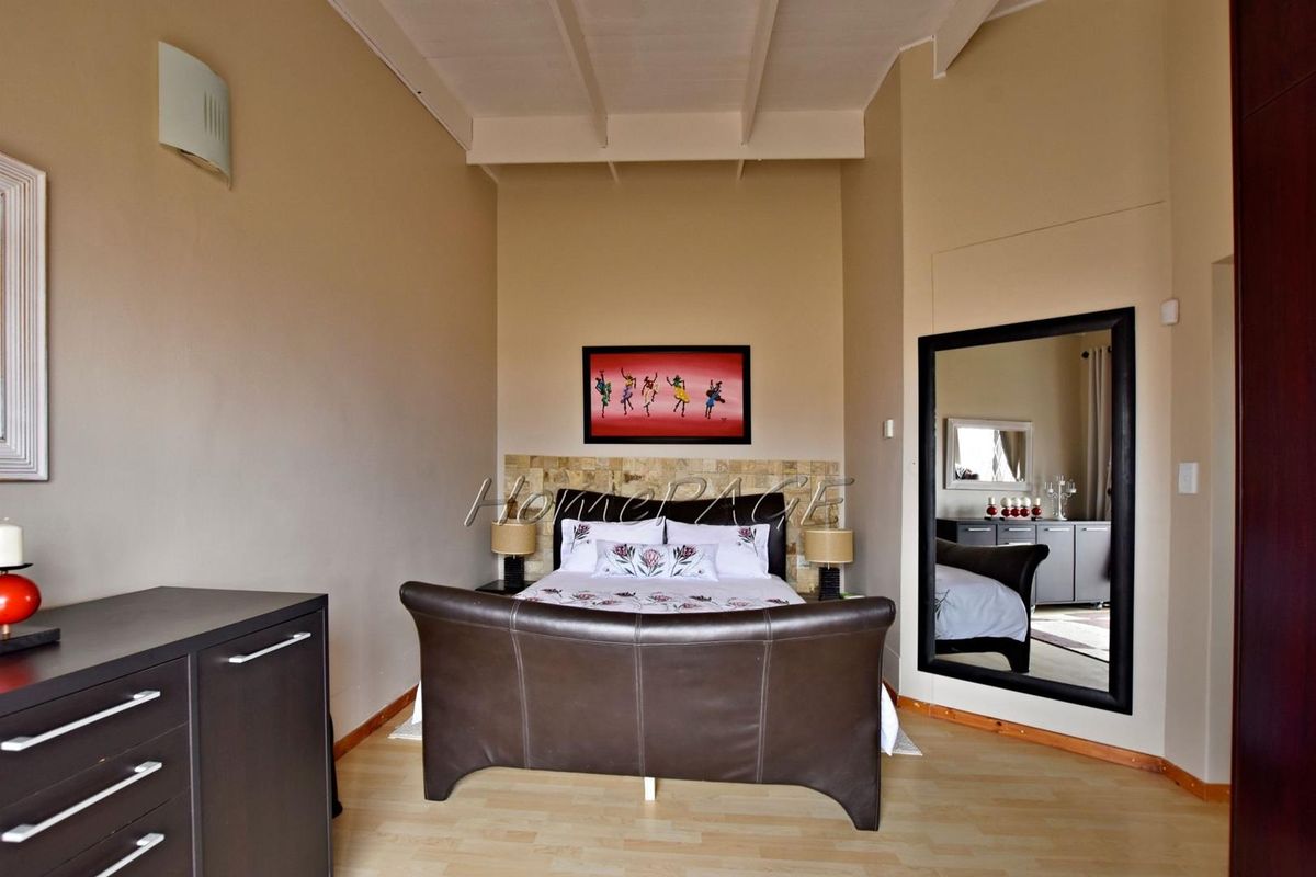 Spacious bedroom featuring high vaulted ceilings with exposed beams, light wood-look flooring, and a decorative stone-tiled feature wall behind the bed area.
