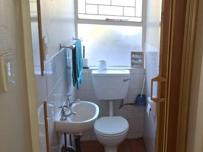 A compact guest bathroom featuring a toilet, wall-mounted basin, tiled finishes, and a sliding door entrance.