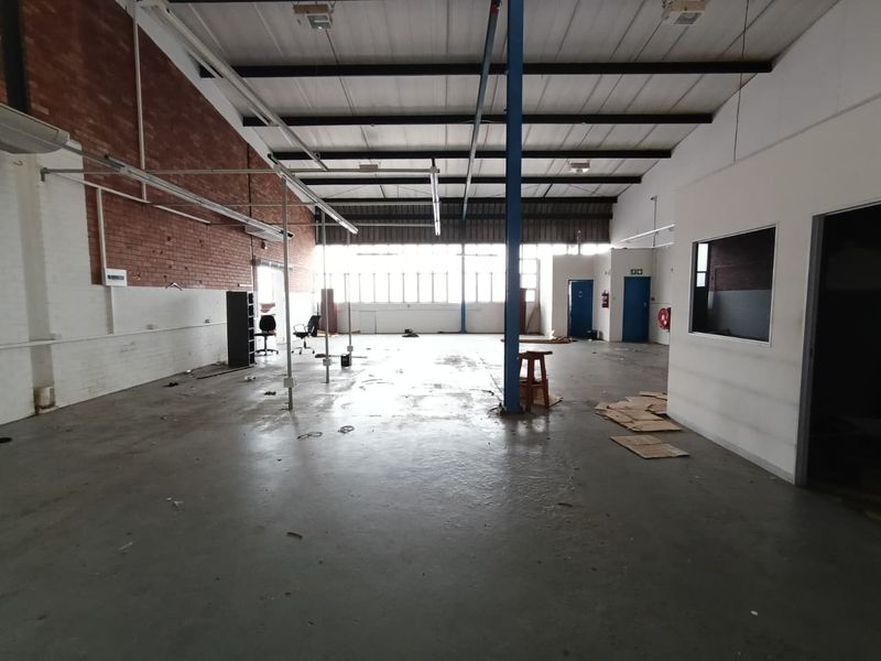 Spacious industrial warehouse unit featuring high ceilings, exposed brickwork, concrete flooring, and a central steel support column, suitable for various commercial or storage uses.