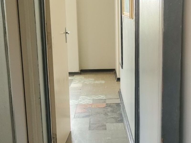 A narrow interior hallway featuring worn tiled flooring and painted door frames, requiring cosmetic updates to improve the overall aesthetic.