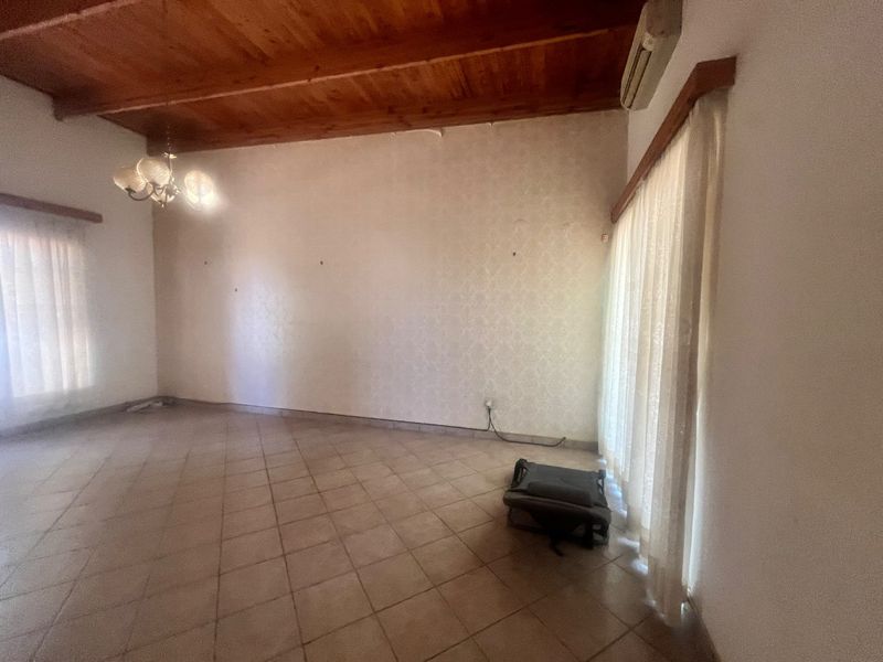 Spacious living area featuring tiled flooring, exposed timber beam ceiling, and a wall-mounted air conditioning unit, offering a blank canvas for interior design.