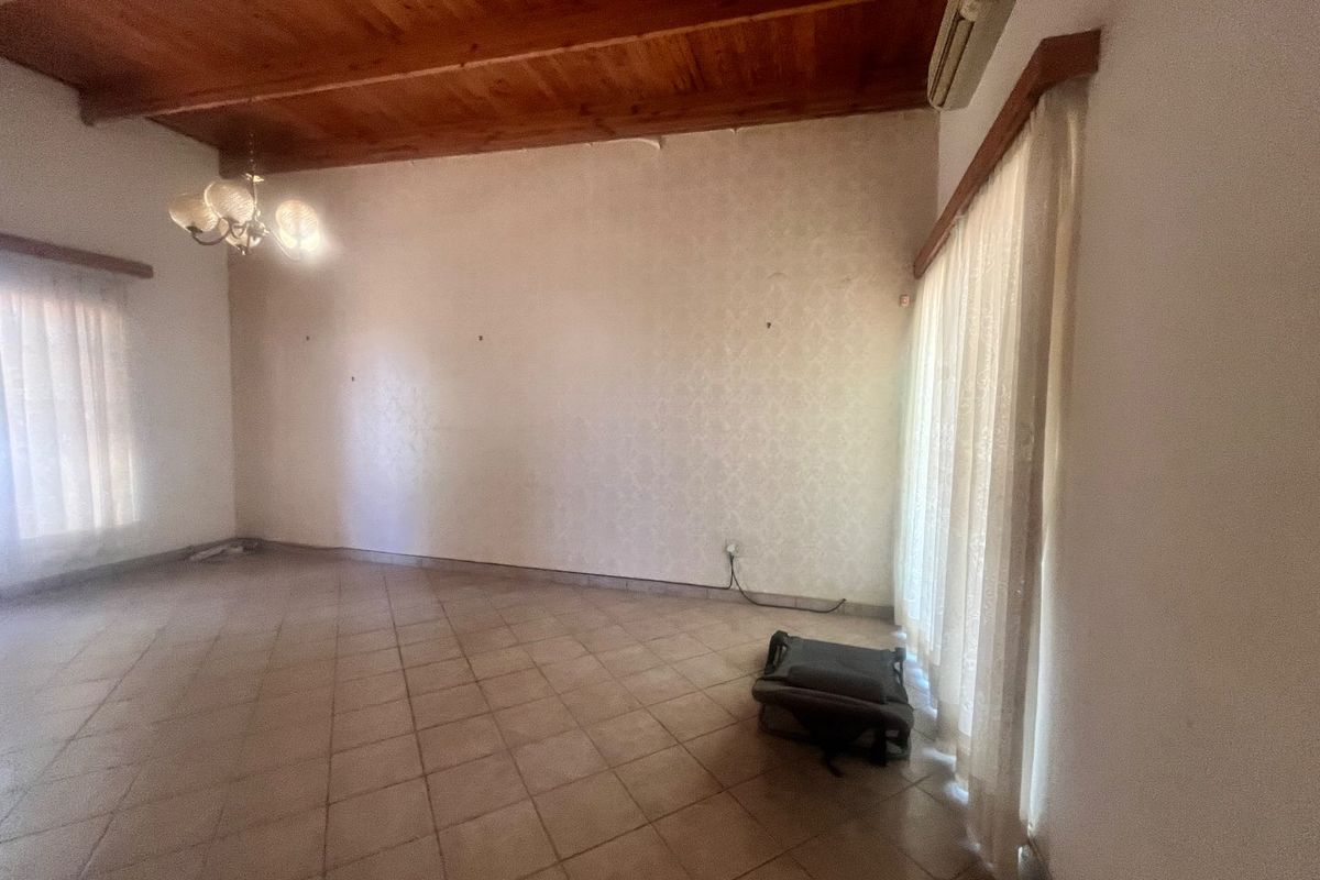 Spacious living area featuring tiled flooring, exposed timber beam ceiling, and a wall-mounted air conditioning unit, offering a blank canvas for interior design.