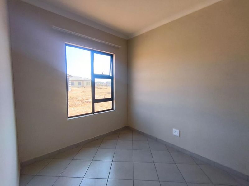 A clean, empty bedroom featuring neutral wall tones, tiled flooring, and a large aluminium-framed window providing natural light.