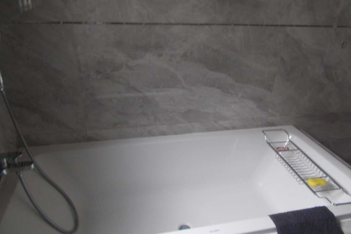 A modern bathroom featuring a clean white bathtub with a handheld shower fixture and elegant grey marble-look wall tiling.