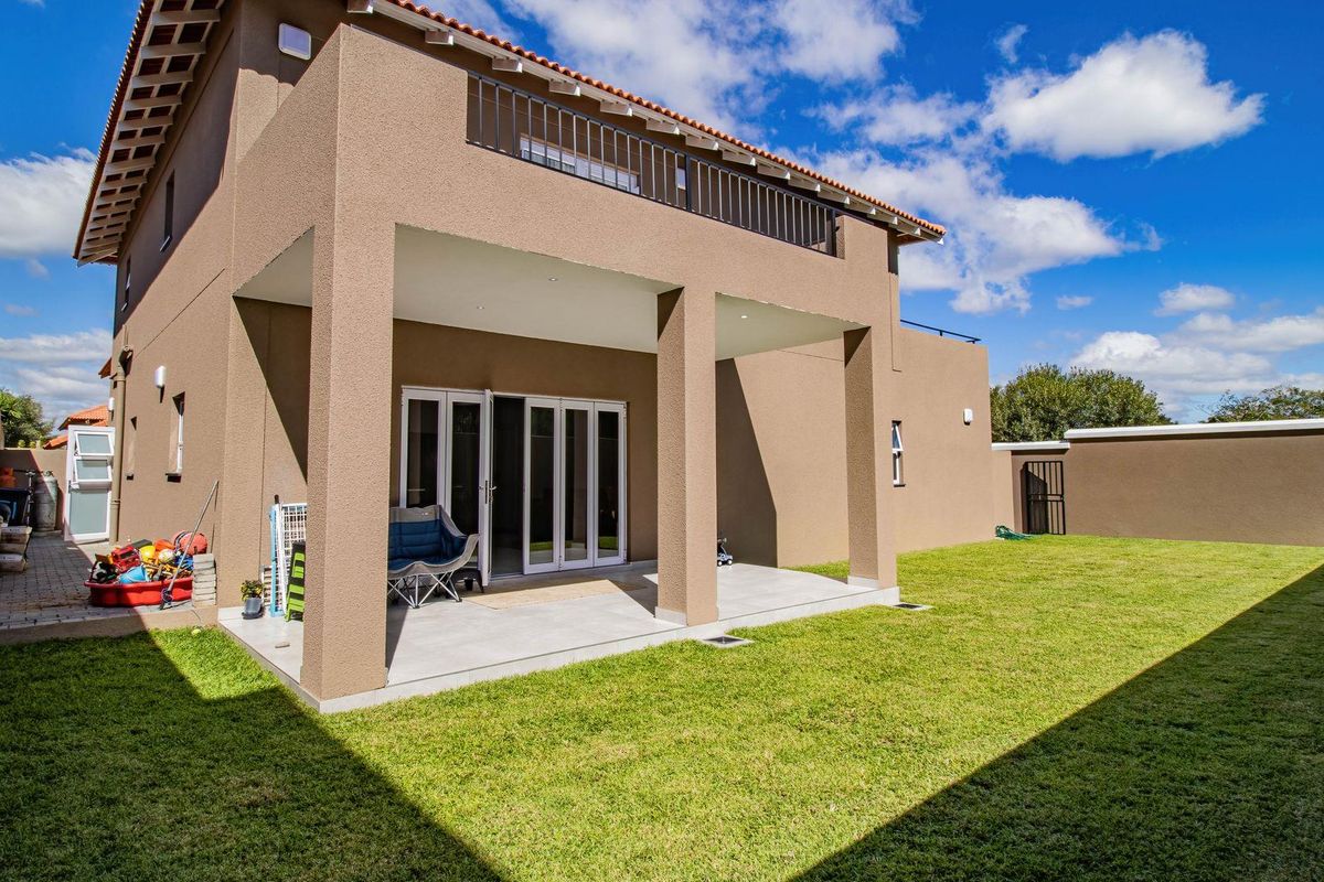 Rear view of the cluster home featuring a covered patio, upper balcony, and a well-maintained private garden with boundary walls.