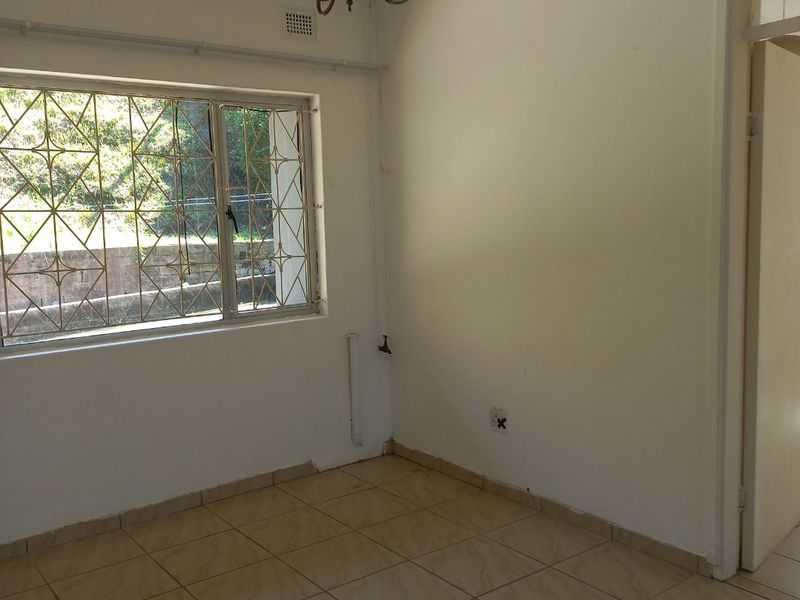 An empty bedroom featuring tiled flooring, a window with metal security bars, and a ceiling light fixture.