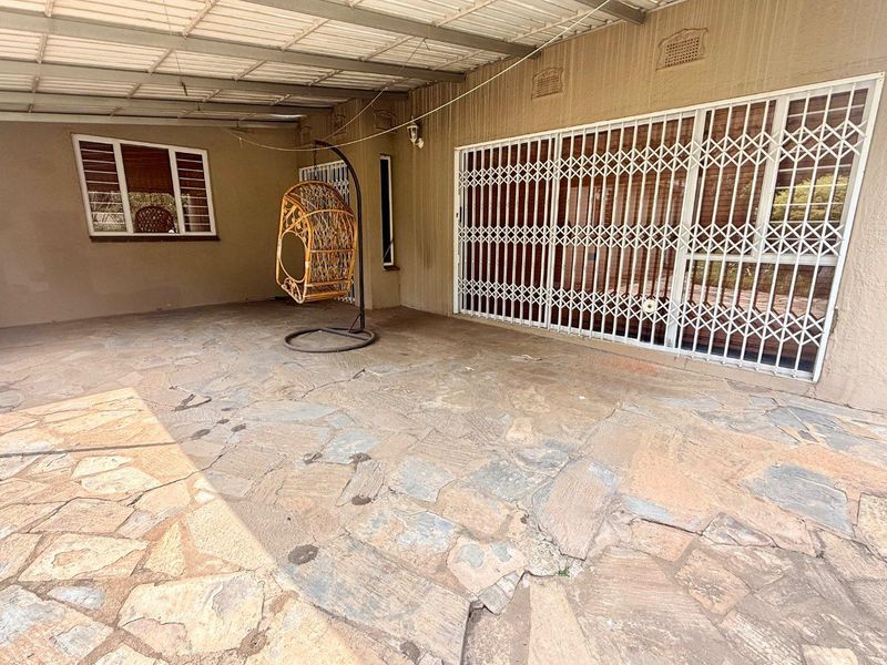 A covered outdoor patio area featuring stone paving, a corrugated metal roof, and secure metal security gates leading into the home.