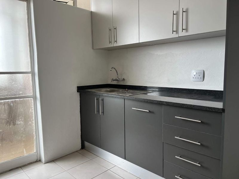 A compact kitchen featuring modern grey and white cabinetry, stone countertops, and a stainless steel sink, ready for final finishing touches.