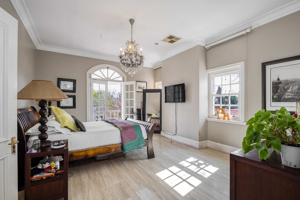 Spacious bedroom featuring light wood-look flooring, crown molding, a classic chandelier, and French doors opening to a private balcony.