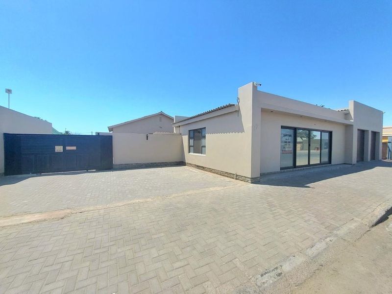 Front exterior view of the property featuring a paved driveway, secure boundary wall, and modern sliding glass entrance doors.