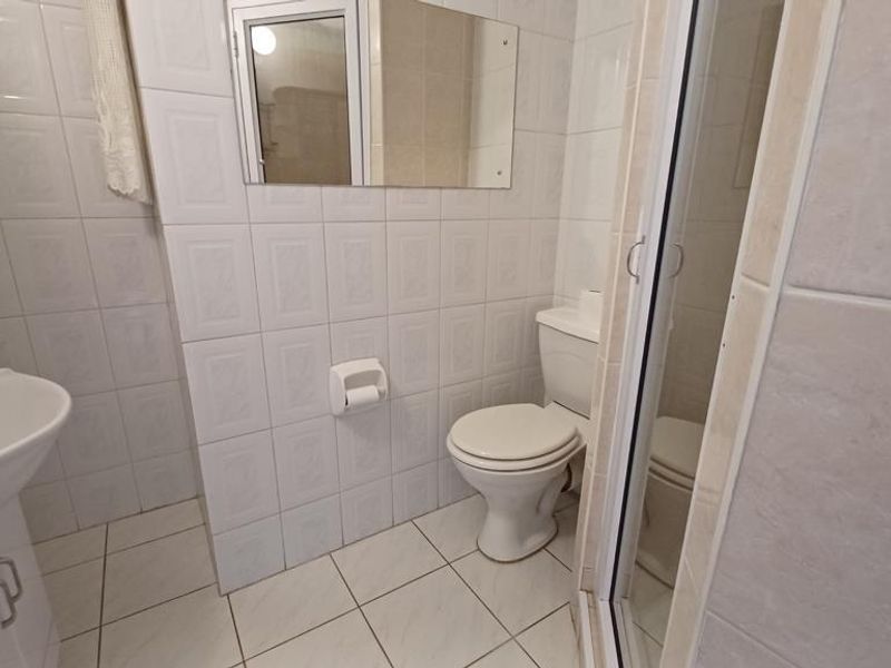 A functional bathroom featuring a vanity basin, toilet, and a glass-enclosed shower, finished with neutral wall and floor tiles.
