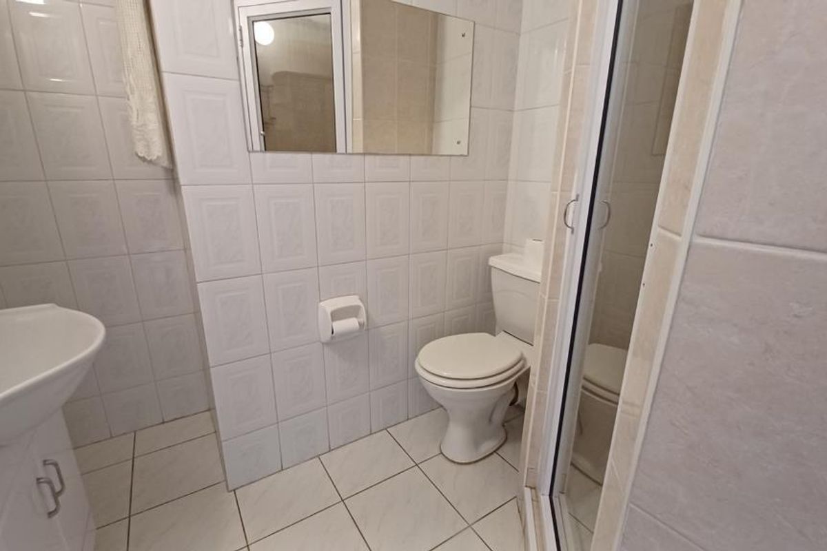 A functional bathroom featuring a vanity basin, toilet, and a glass-enclosed shower, finished with neutral wall and floor tiles.