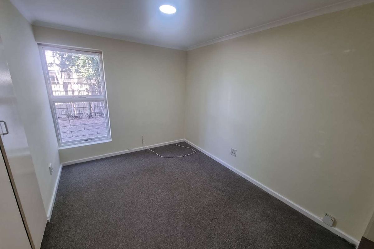 An empty bedroom featuring neutral walls, carpet flooring, a built-in cupboard, and a window providing natural light.