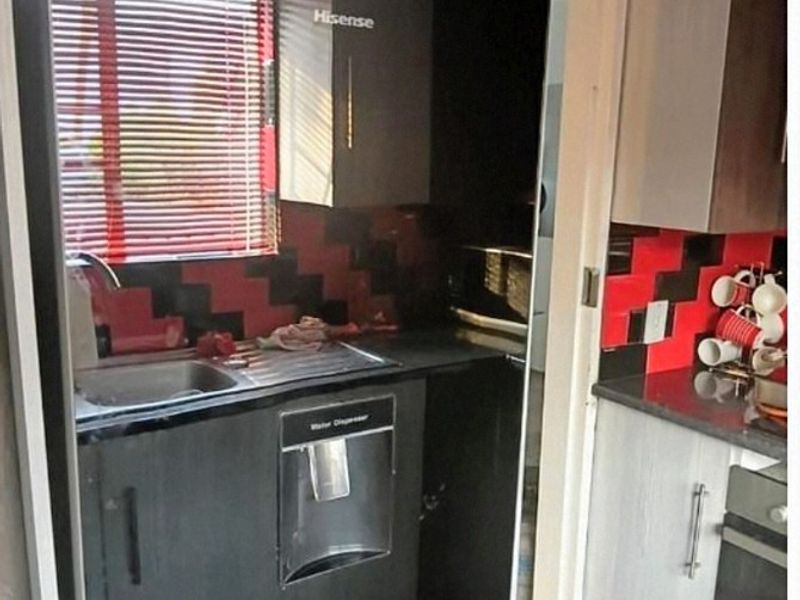 A compact kitchen featuring built-in cabinetry, a stainless steel sink, integrated oven, and a distinctive red and black tiled backsplash.