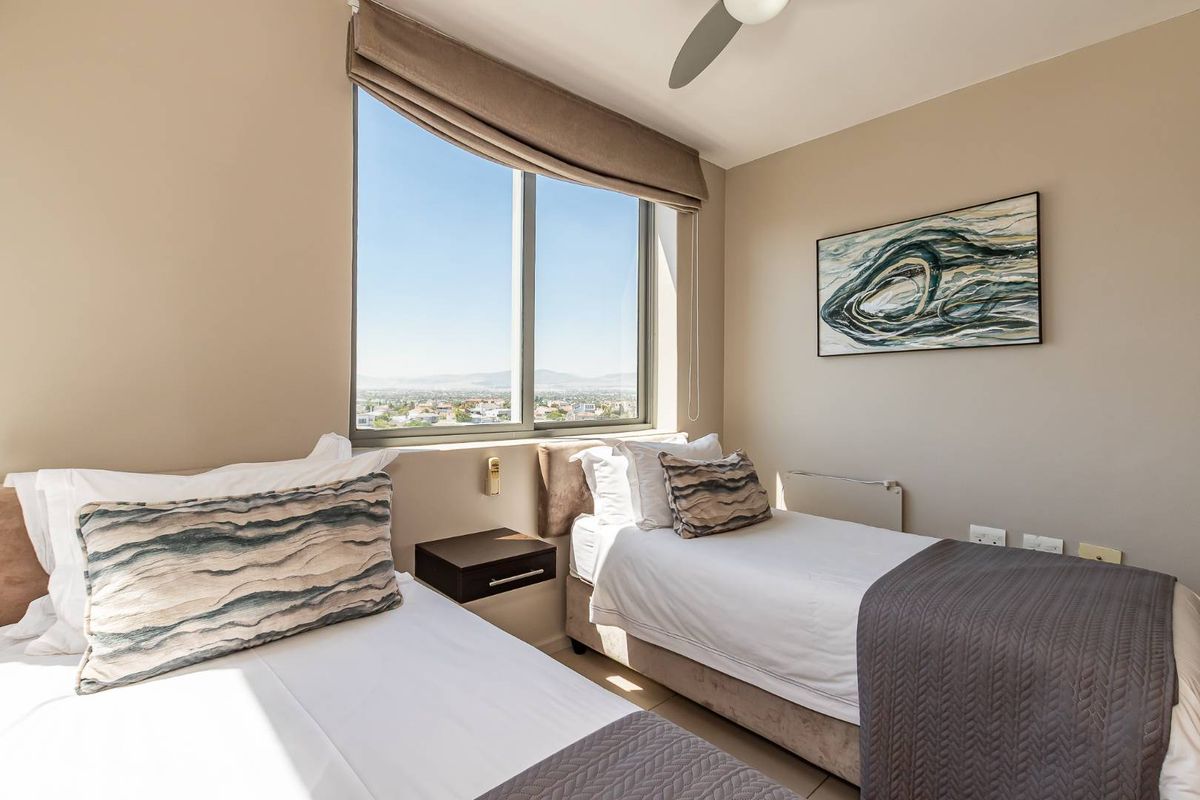 A well-lit bedroom featuring a large window with expansive city views, a ceiling fan, and neutral wall finishes.