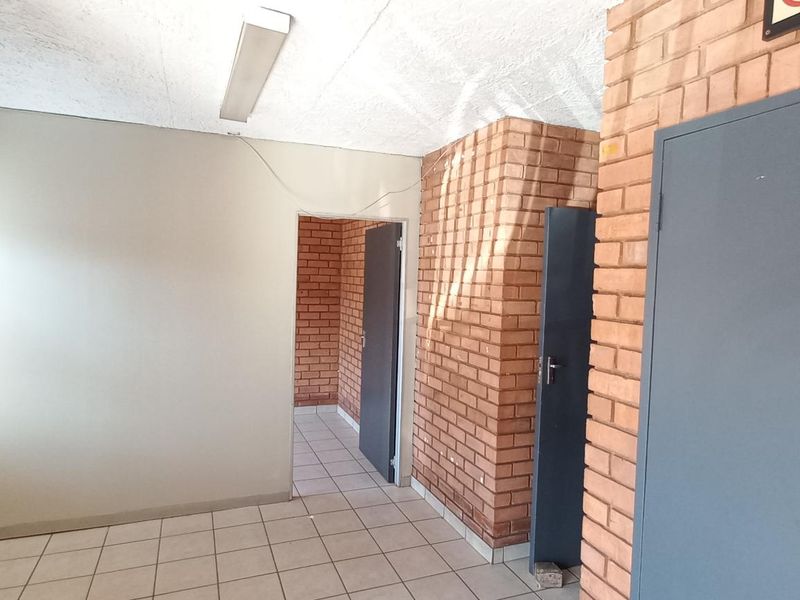 An interior office or utility space featuring exposed brick walls, tiled flooring, and multiple doorways leading to adjacent rooms.