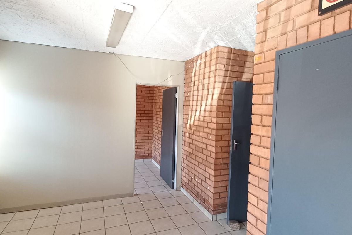 An interior office or utility space featuring exposed brick walls, tiled flooring, and multiple doorways leading to adjacent rooms.