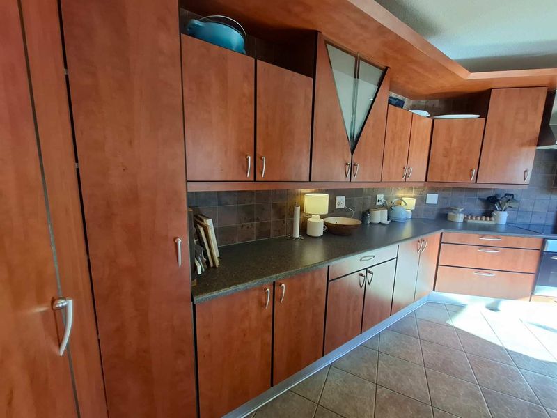 A functional kitchen featuring wood-tone cabinetry, dark laminate countertops, tiled backsplash, and ceramic floor tiles with a built-in oven.