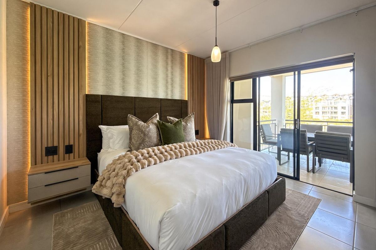 Modern bedroom featuring timber slat wall paneling with integrated LED lighting, tiled floors, and direct access to a private balcony through sliding glass doors.