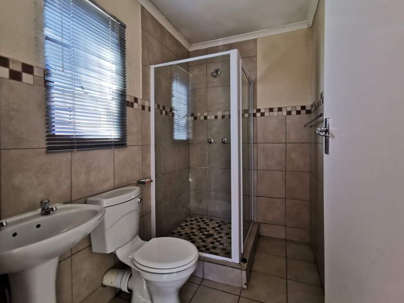 A functional bathroom featuring a shower enclosure, pedestal basin, and toilet with neutral wall and floor tiling.