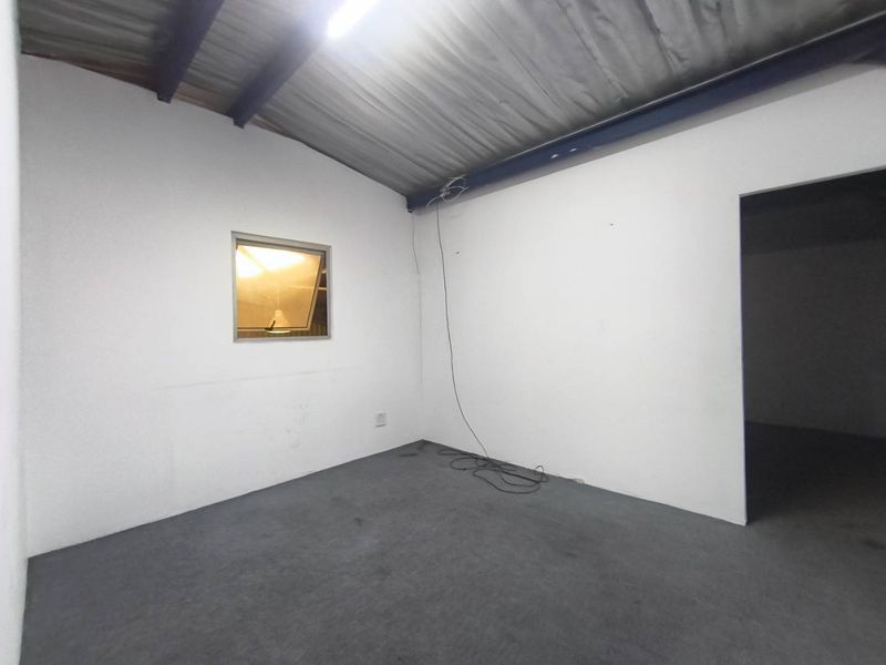 A functional industrial utility space featuring exposed steel roof beams, corrugated metal ceiling, and an awning window, suitable for storage or workspace.