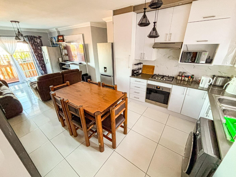 Open-plan living area featuring a modern kitchen with built-in cabinetry, gas hob, and tiled flooring, seamlessly flowing into the dining and lounge space.