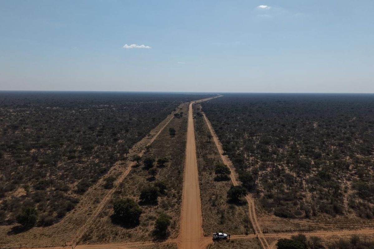An aerial view of a long dirt road stretching through expansive, undeveloped farm land with natural vegetation.