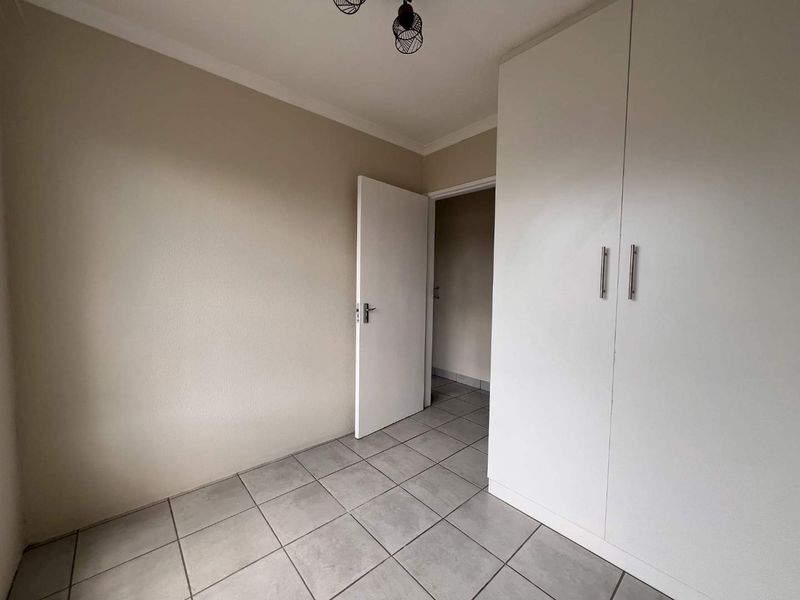 A clean, empty bedroom featuring neutral wall paint, tiled flooring, and a built-in white wardrobe with modern handles.