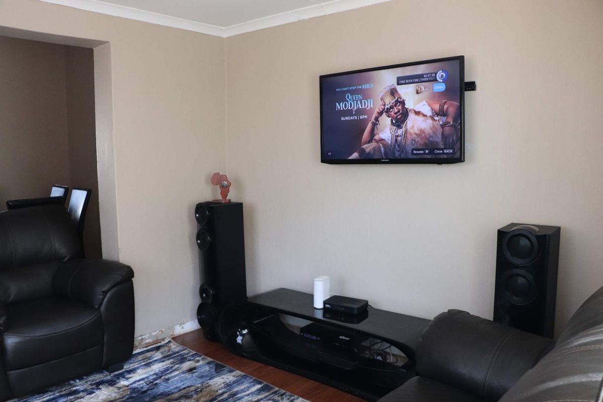 A living room area featuring laminate flooring and coved ceilings, currently showing missing skirting boards along the base of the wall.