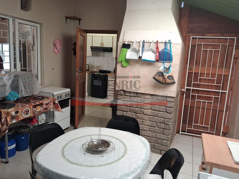 Open plan living area featuring a brick fireplace and tiled flooring, with an adjacent kitchen visible through the doorway.