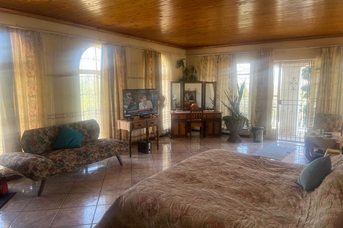 Spacious bedroom featuring a warm timber tongue and groove ceiling, ceramic tiled flooring, and large arched windows providing ample natural light.