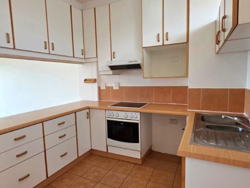 A functional kitchen featuring laminate countertops, built-in oven with electric hob, extractor fan, and a stainless steel double sink with tiled backsplash.