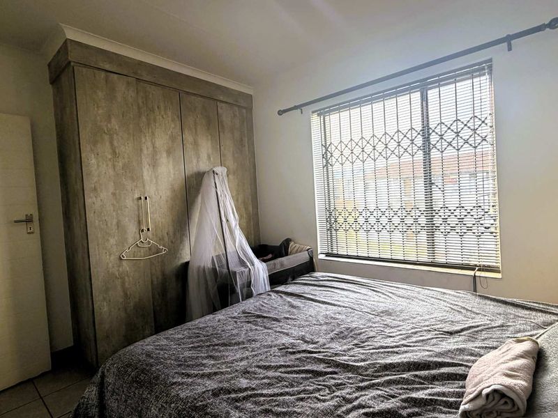 A well-maintained bedroom featuring built-in cupboards, tiled flooring, and a window fitted with security gates and venetian blinds.