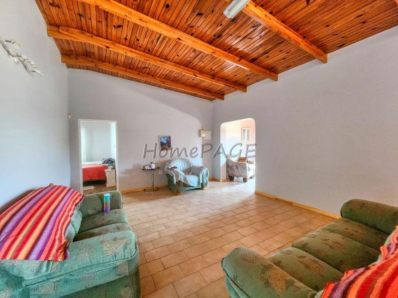 Spacious living room featuring a vaulted timber beam ceiling and tiled flooring, with an open archway leading to adjacent rooms.