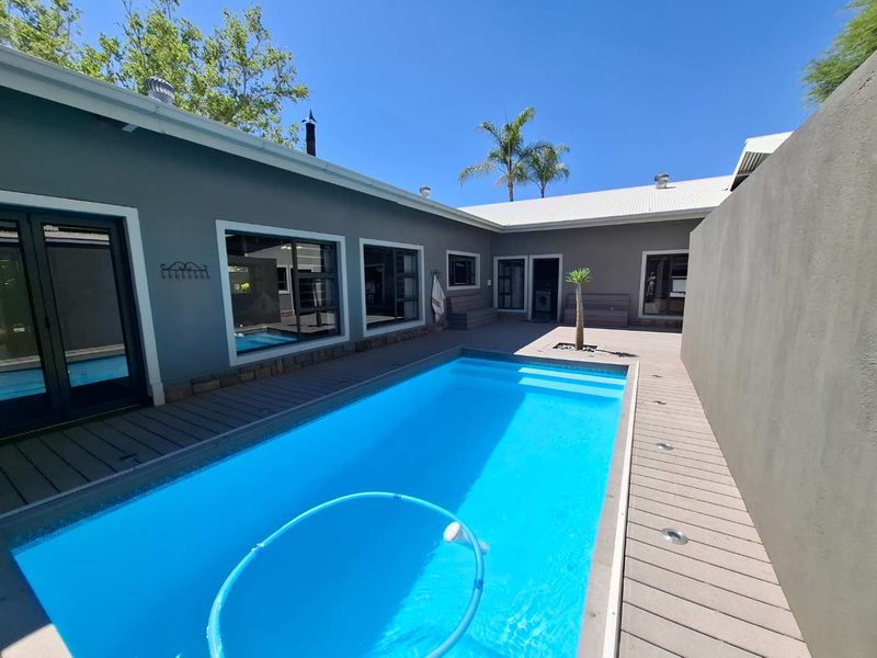 A well-maintained outdoor pool area featuring modern composite decking, recessed lighting, built-in bench seating, and direct access to the home's living spaces.