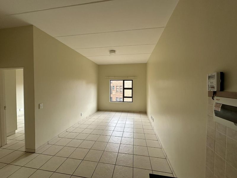 A spacious, empty living area featuring neutral tiled flooring, clean walls, and a large window providing natural light.