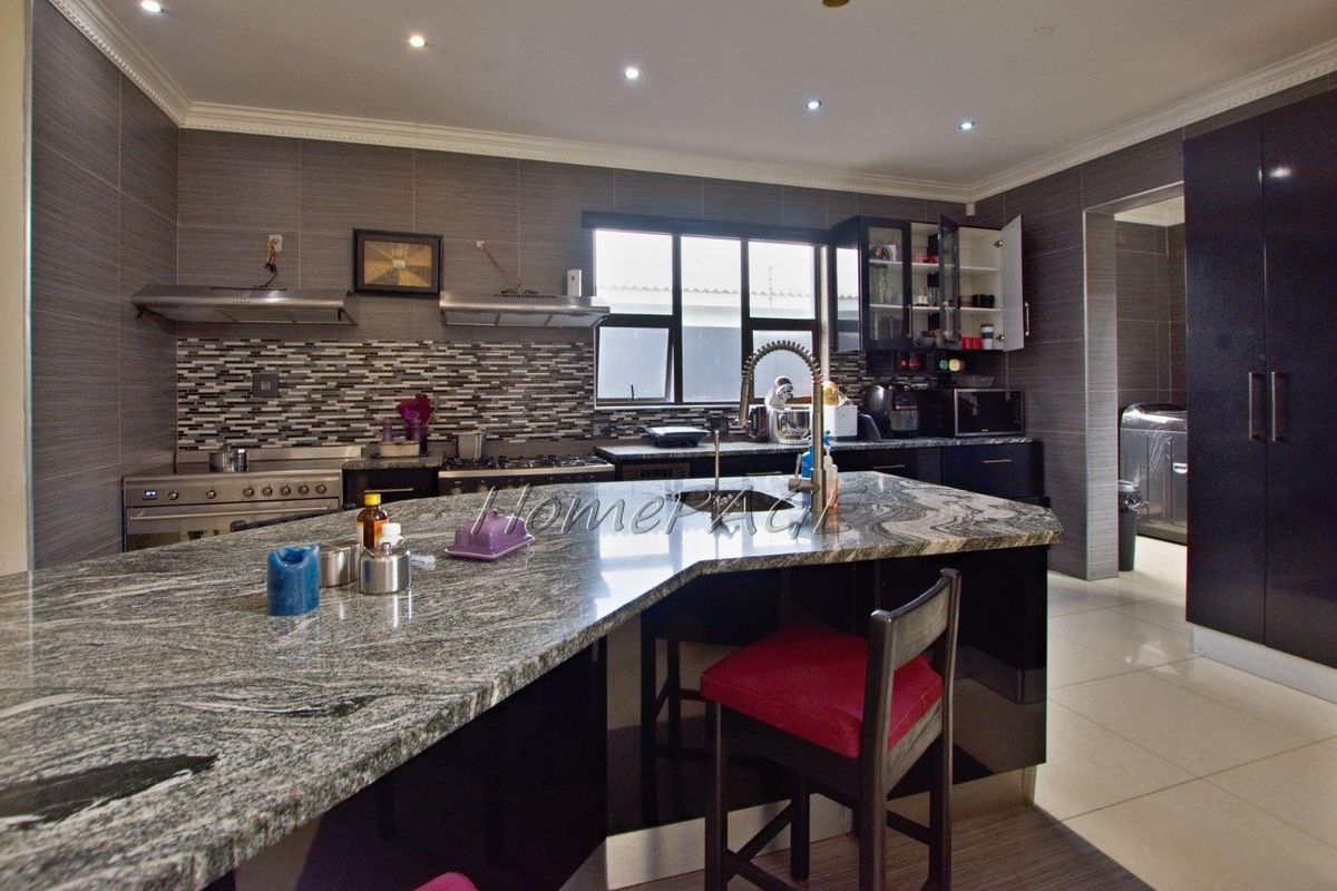 Modern kitchen featuring a large granite-topped island, built-in gas stove, stainless steel extractor fan, and tiled splashback with ample cabinetry.